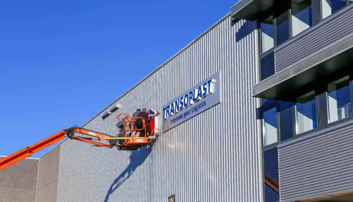 Installatie van verlichte doosletters op een bedrijfspand met hoogwerker.