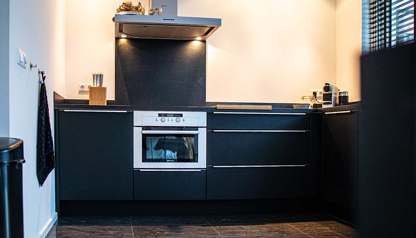Een stijlvolle zwarte keuken met een ingebouwde oven, rvs-afzuigkap en sfeervolle verlichting, volledig gewrapped voor een luxe uitstraling.