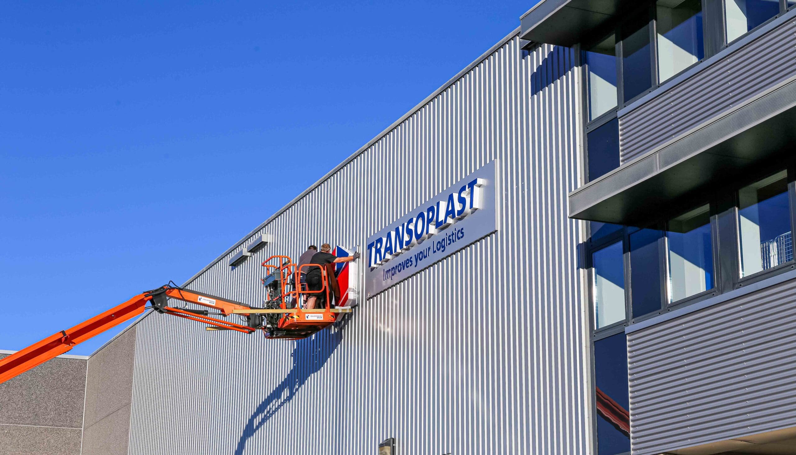 Installatie van verlichte doosletters op een bedrijfspand met hoogwerker.